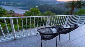 Ein Balkon mit zwei schwarzen Stühlen und einem weißen Geländer, der einen malerischen Blick auf einen See und Berge bietet.