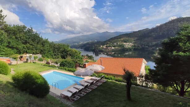 Ein Pool mit Liegestühlen und Sonnenschirmen, umgeben von üppiger Vegetation und einem See.
