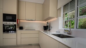 Eine moderne Küche mit weißen Schränken, einem eingebauten Backofen, einer Kaffeemaschine und einem Fenster mit Blick auf Grünflächen.
