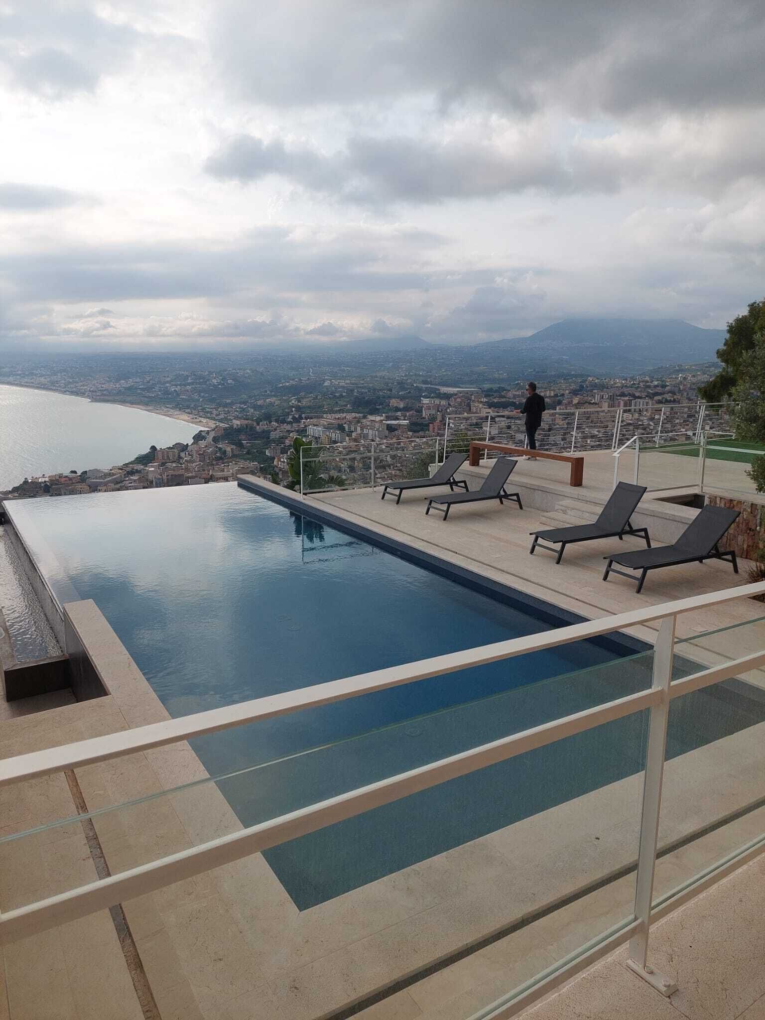 Piscina infinita en la azotea con sillones de descanso y vistas a un paisaje urbano y montañas.
