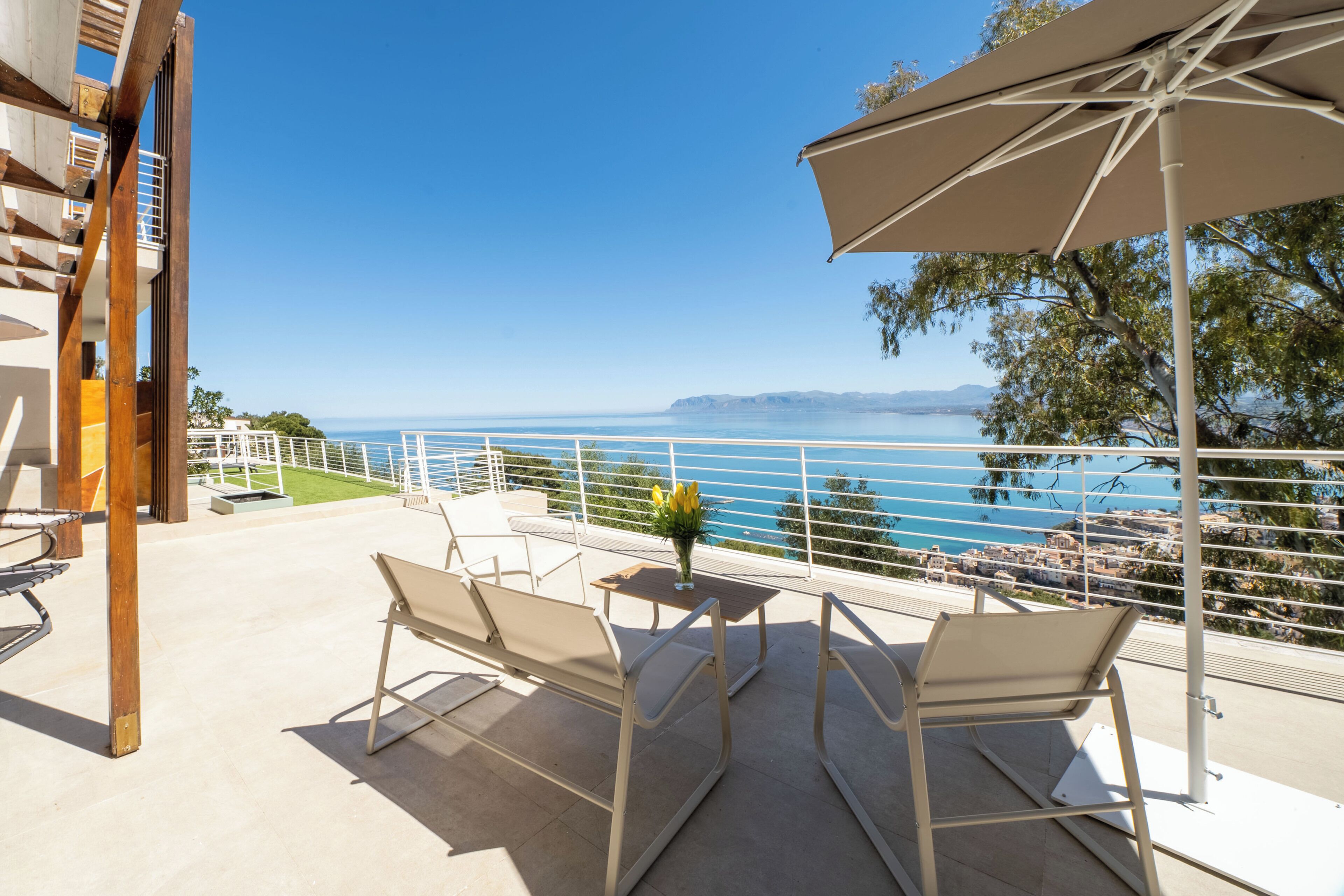 An outdoor seating area with a view of the sea, a table with a vase of flowers, and a large umbrella.
