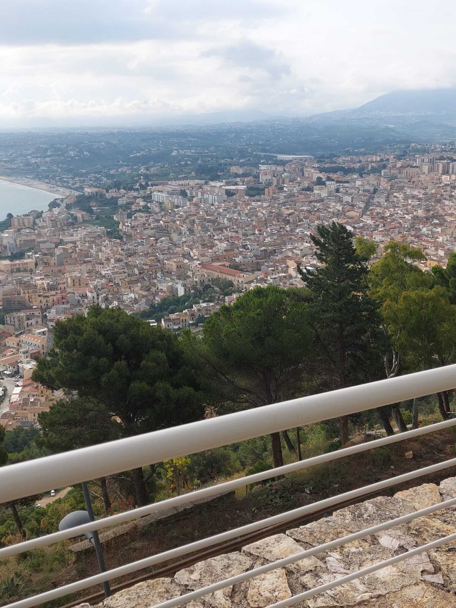 A panoramic view of a coastal city with dense urban architecture, a beach, and a mountainous backdrop.