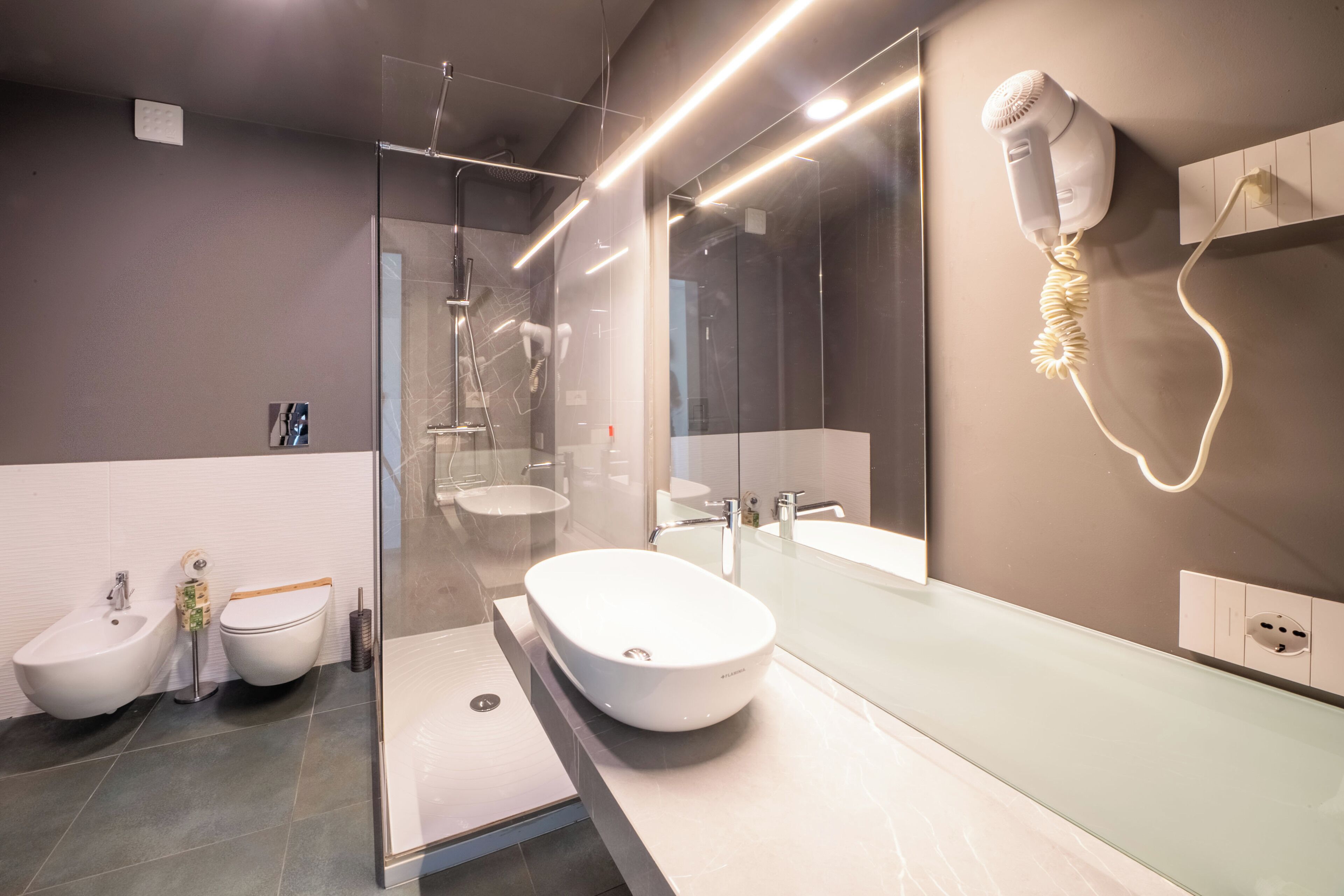 Un baño moderno con cabina de ducha de vidrio, un bidé, un espejo grande y un secador de pelo montado en la pared.
