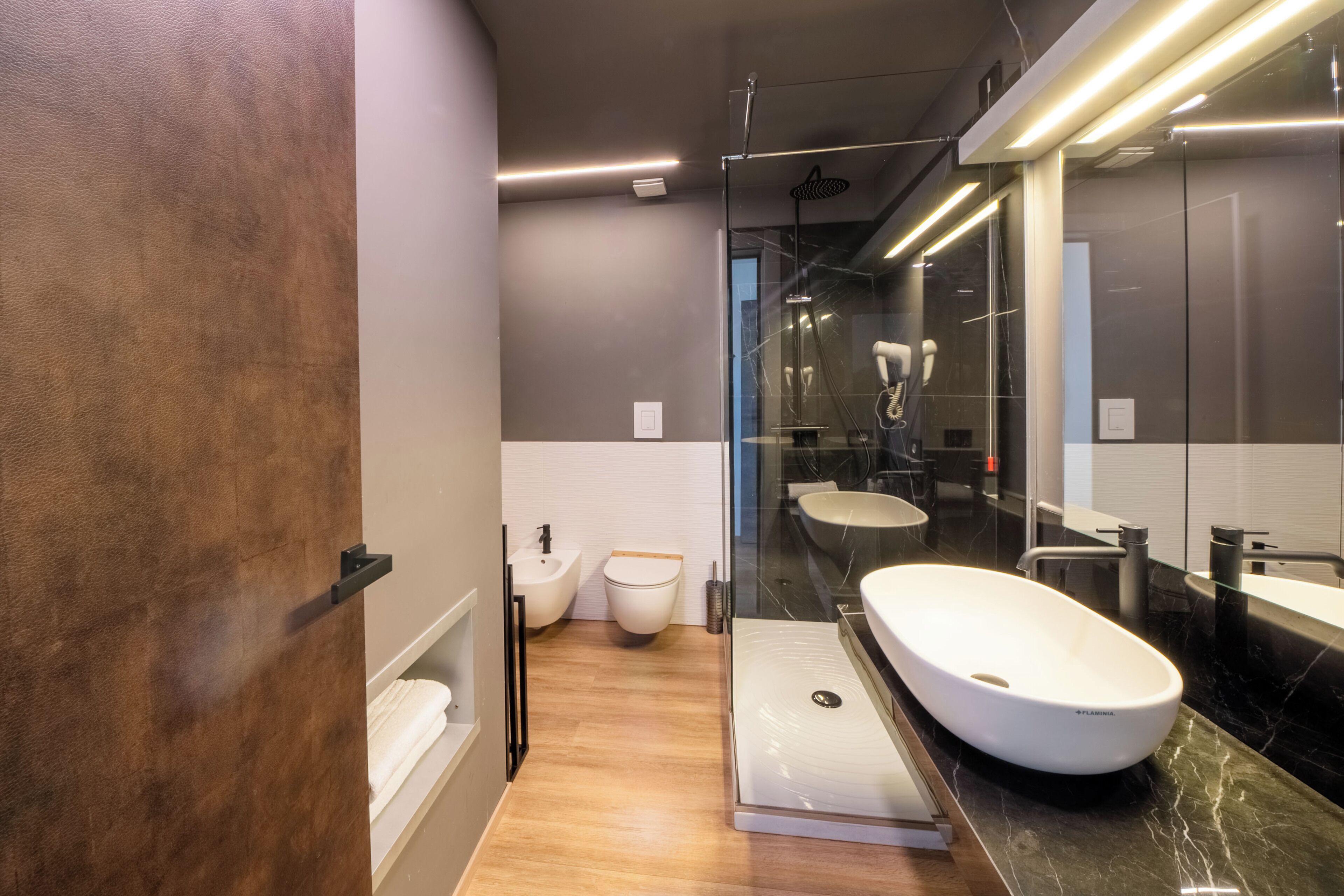 A modern bathroom with a glass shower enclosure, a white vessel sink, and a bidet.