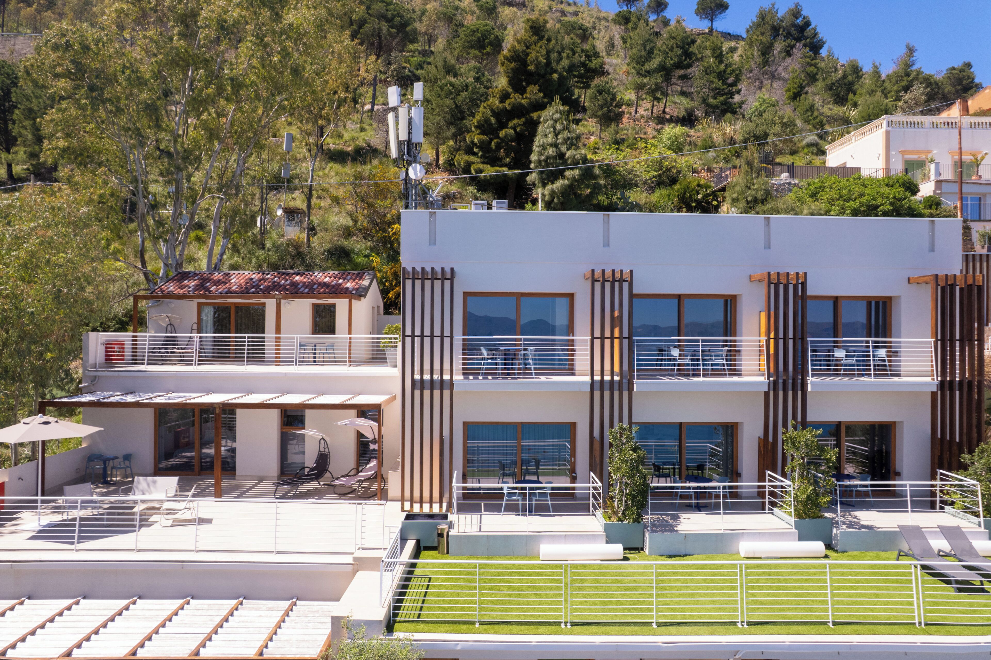 A modern two-story building with a rooftop terrace, large windows, and a balcony.