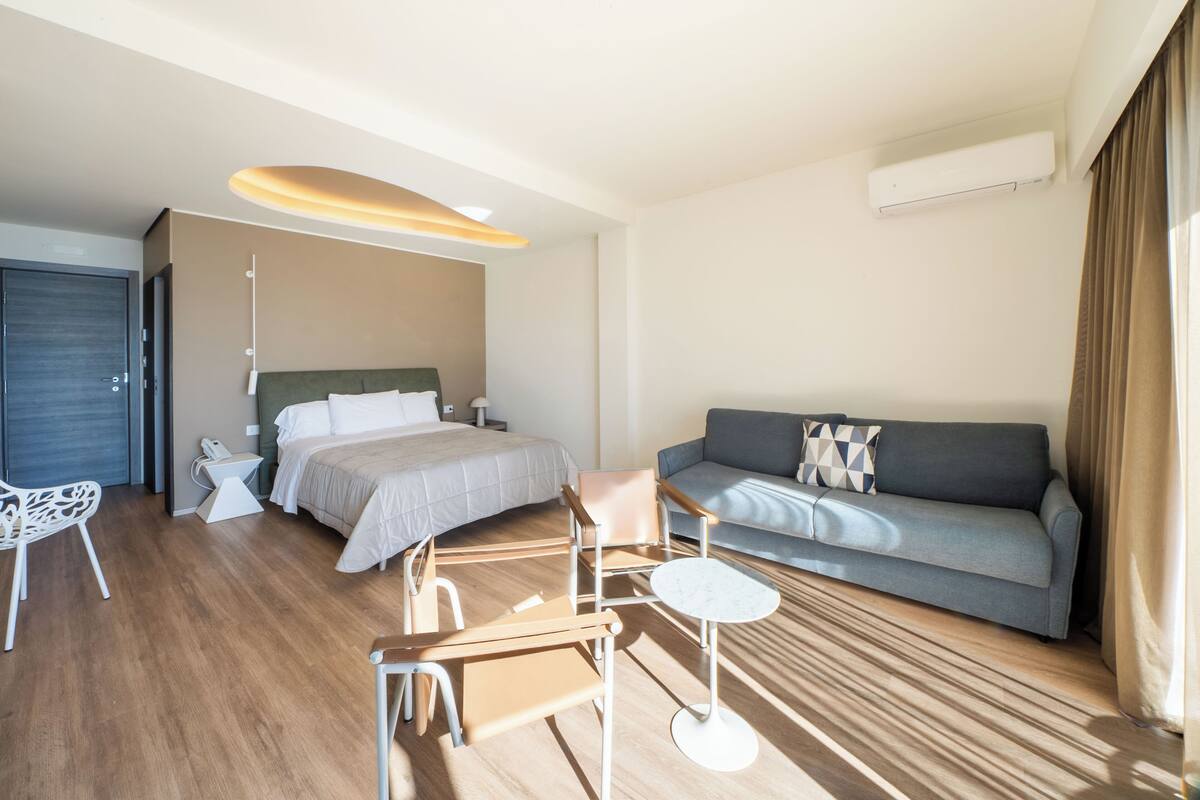 Ett modernt hotellrum med en säng, soffa, skrivbord, stol och ett litet bord.