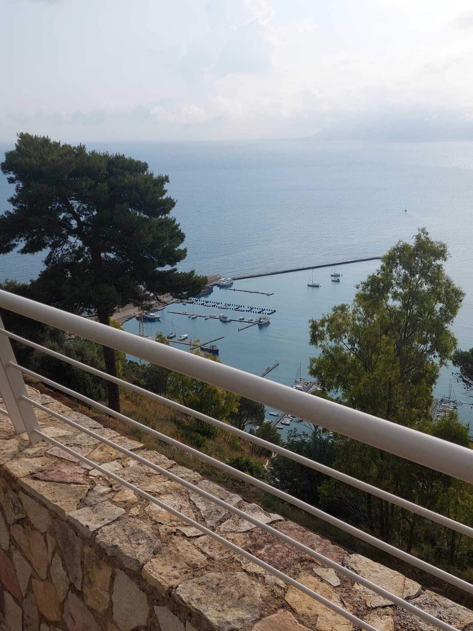 Uitzicht op de kust met een stenen balustrade, een jachthaven met boten en een heldere lucht.