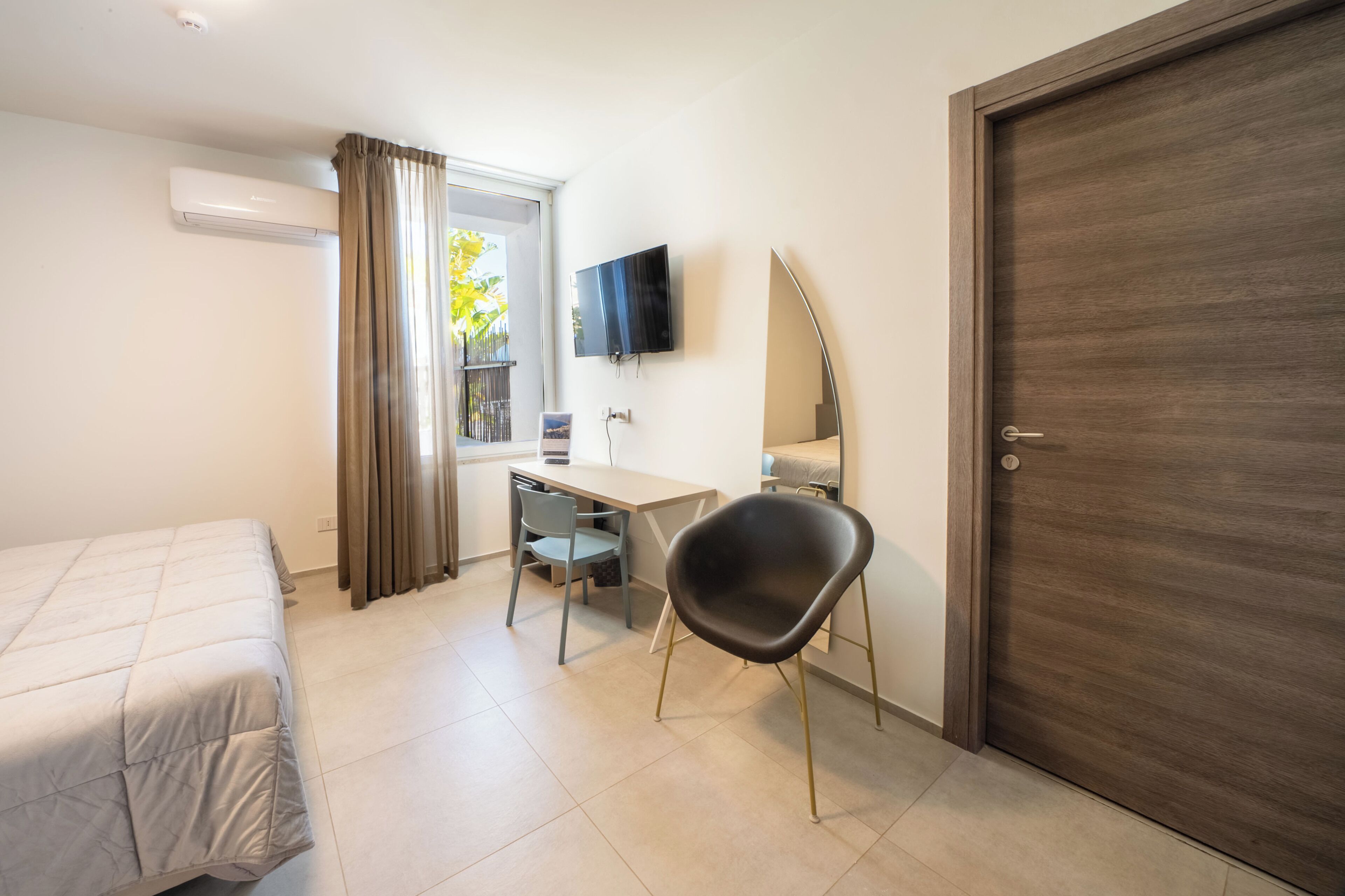 Un dormitorio con una cama, un escritorio, una silla, un televisor y una puerta.