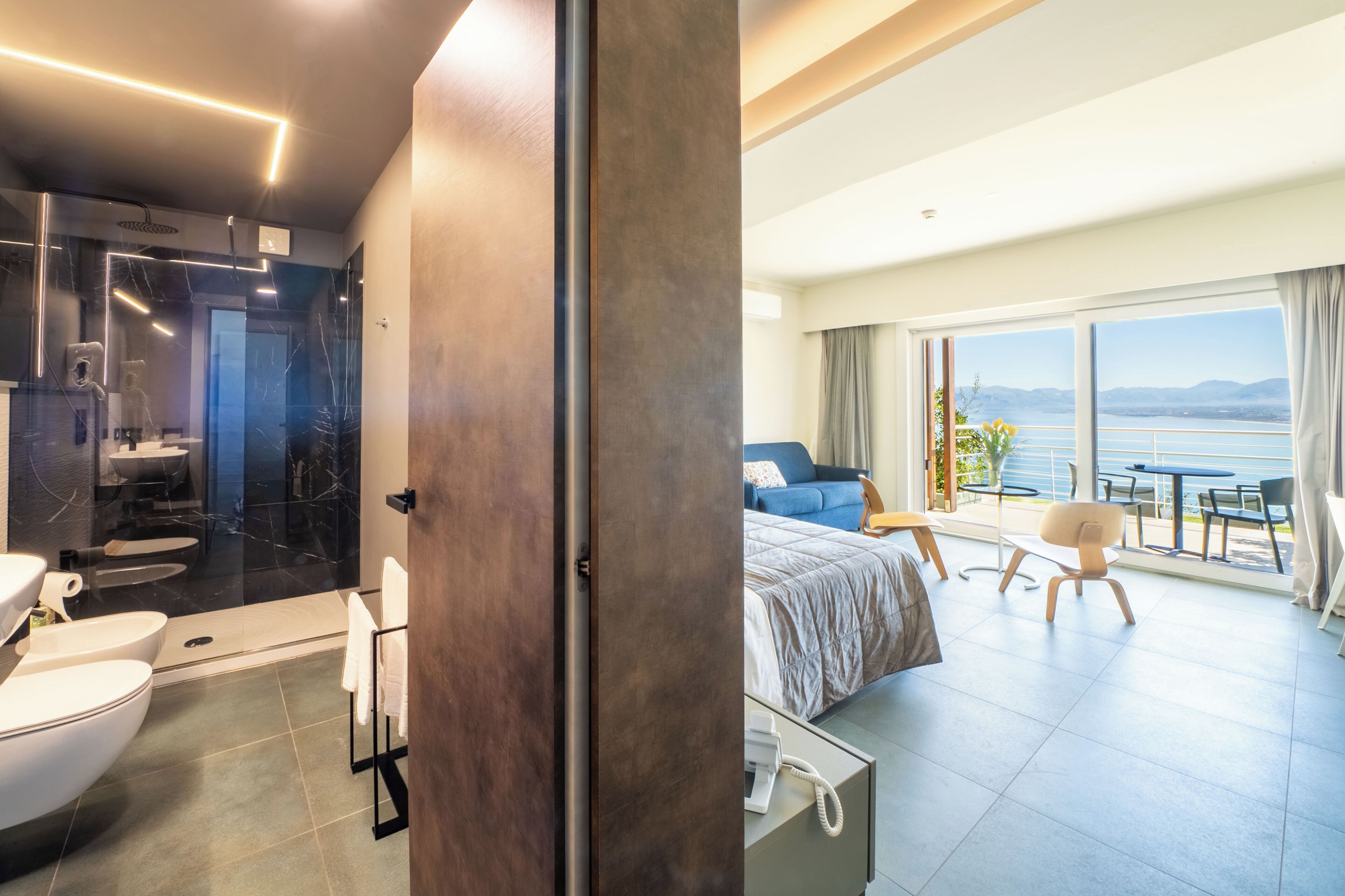 A modern hotel room with a bathroom, a balcony with a view, and a bed.