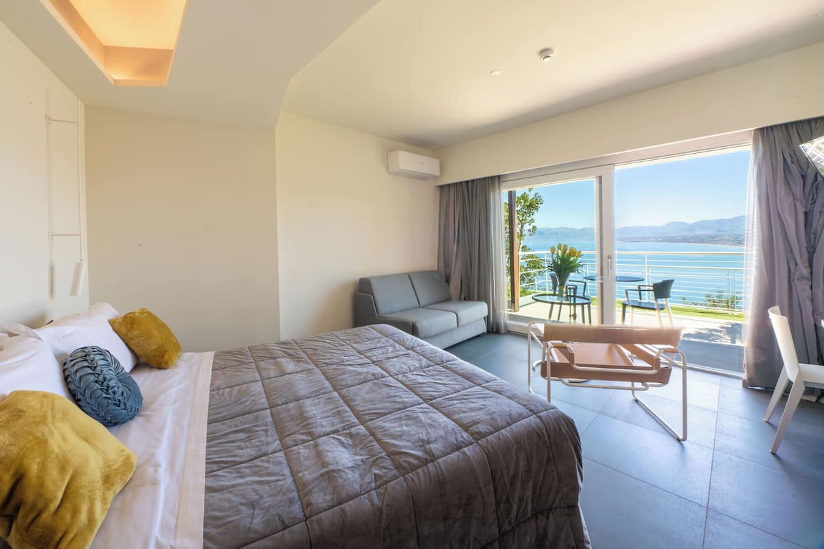Ett hotellrum med en säng, en soffa, ett matbord och utsikt över havet.