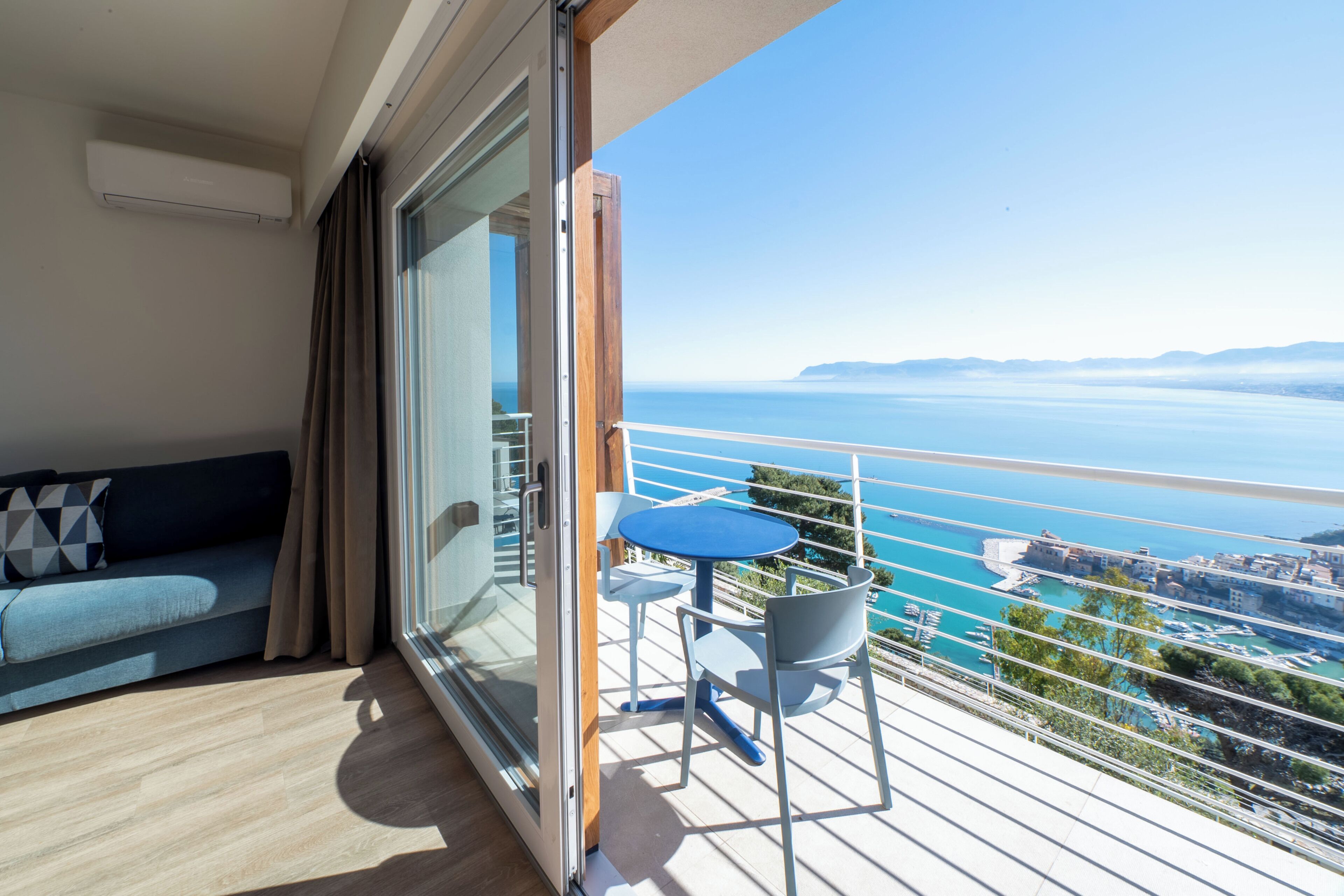 A balcony with a view of the sea, a sofa, and a small table with chairs.