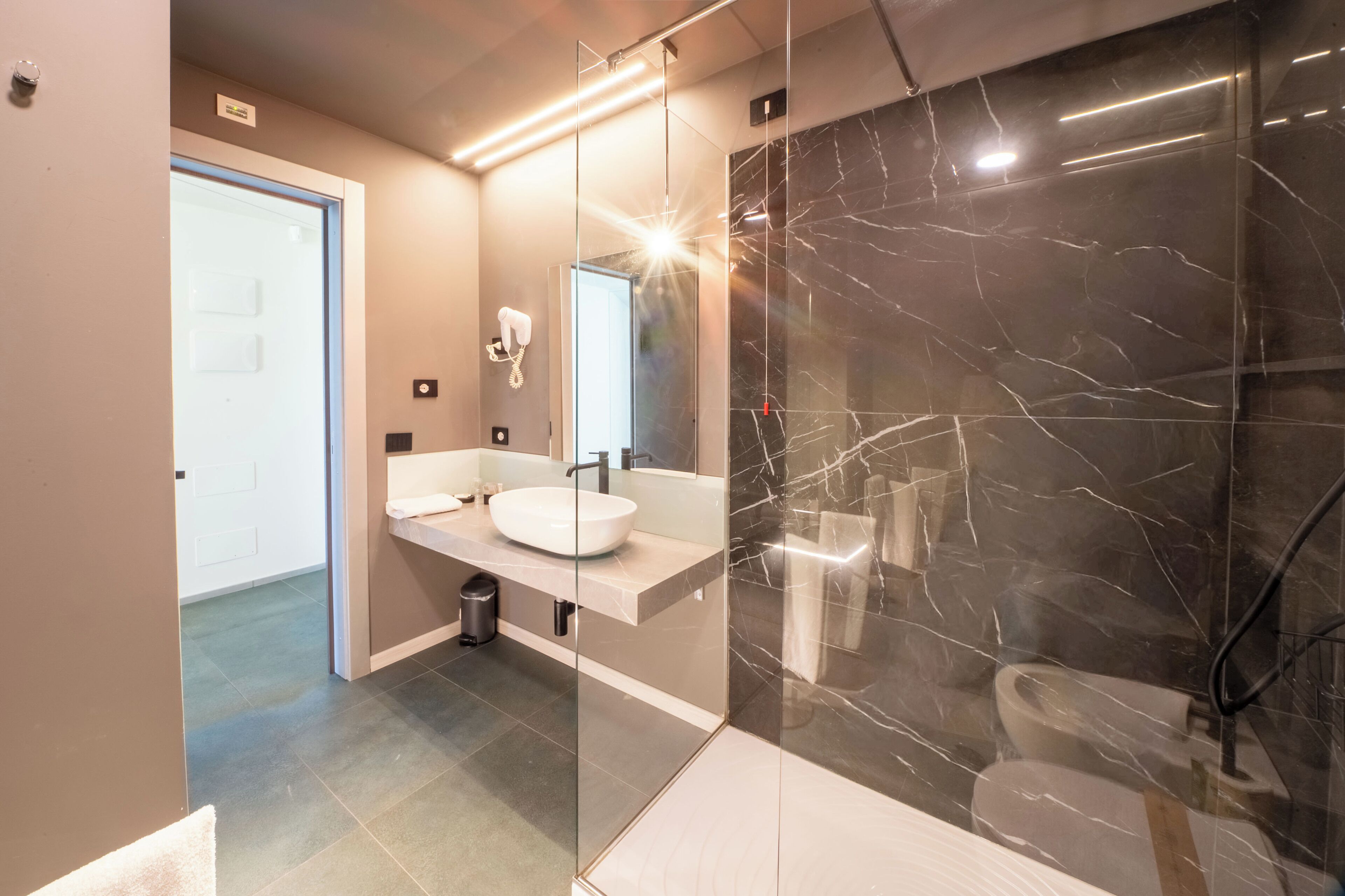 A modern bathroom with a glass-enclosed shower, a white sink, and a marble wall.