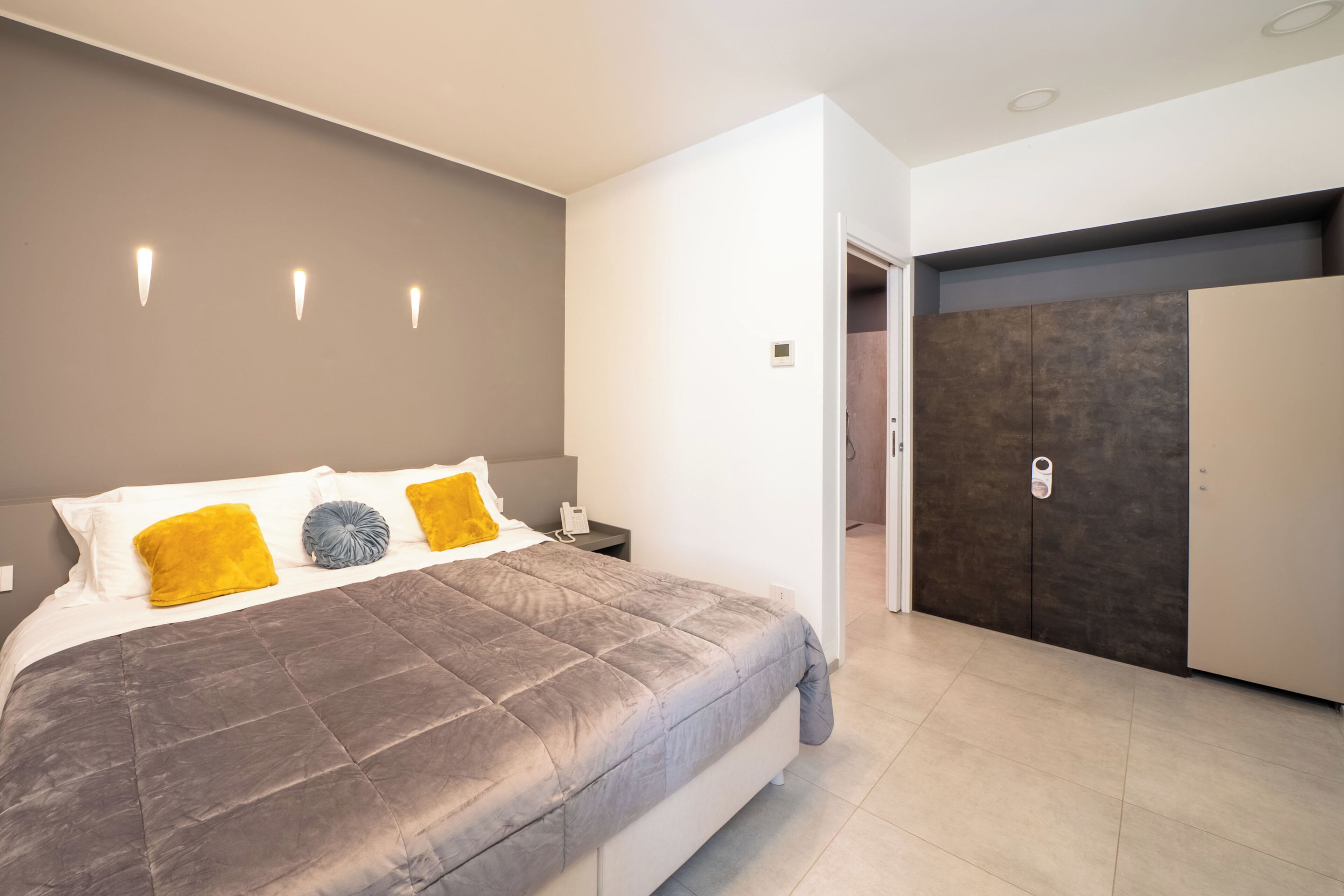 A modern bedroom with a large bed, a wardrobe, and a door leading to another room.