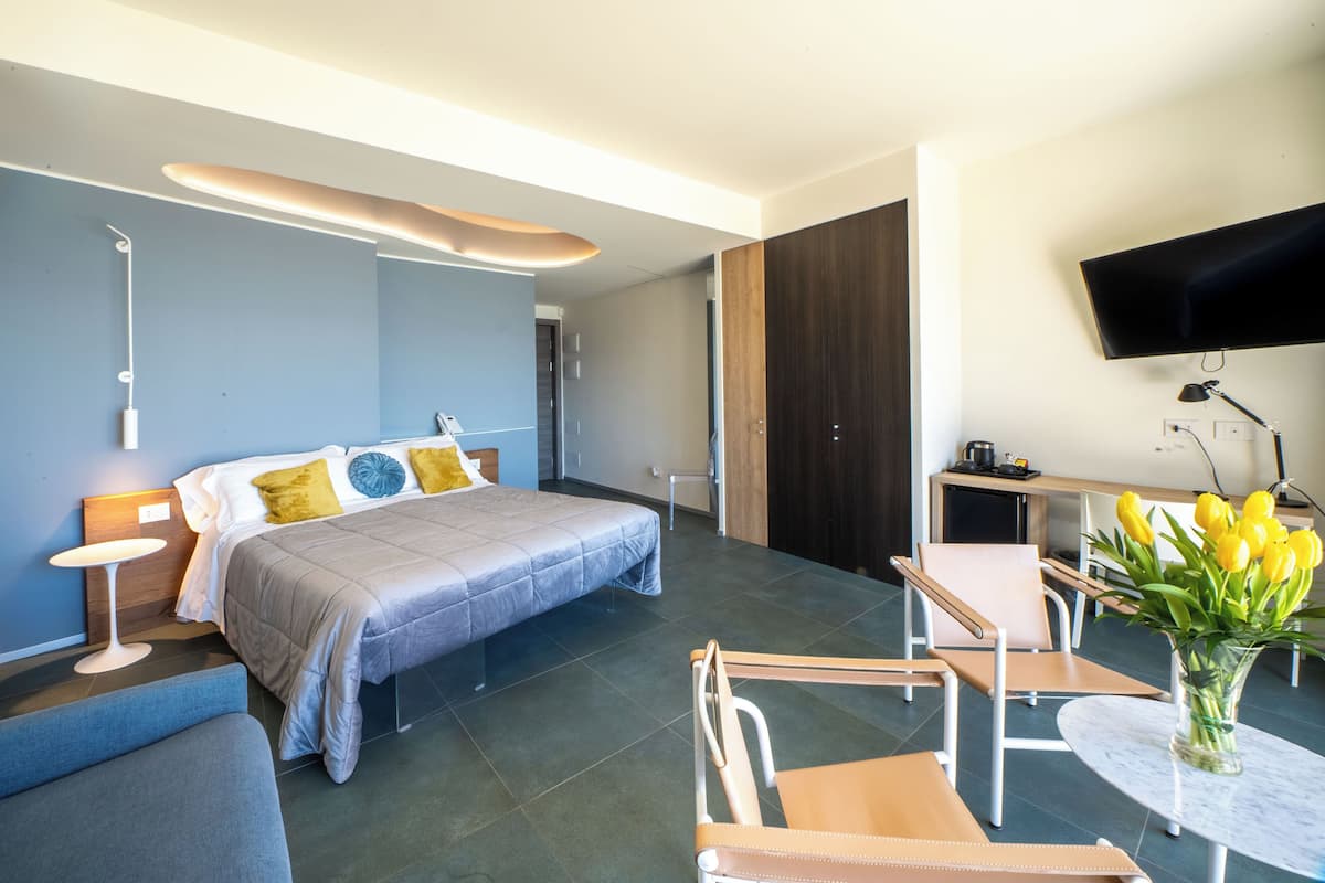 Ett modernt hotellrum med en säng, en sittgrupp, en TV och en vas med blommor.