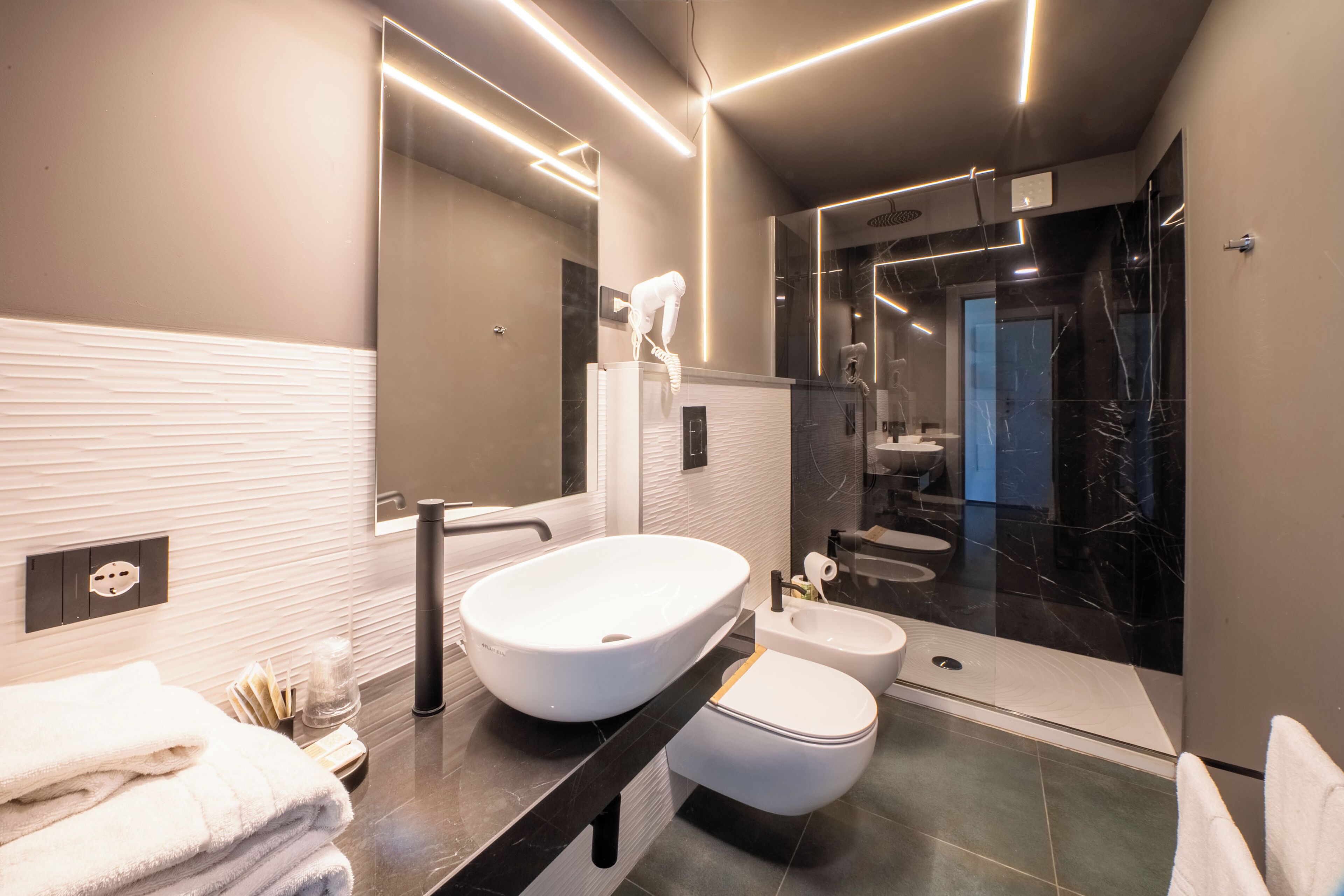 Une salle de bain moderne dotée d’un grand miroir, d’un lavabo sur colonne, d’un bidet et d’une douche à l’italienne.