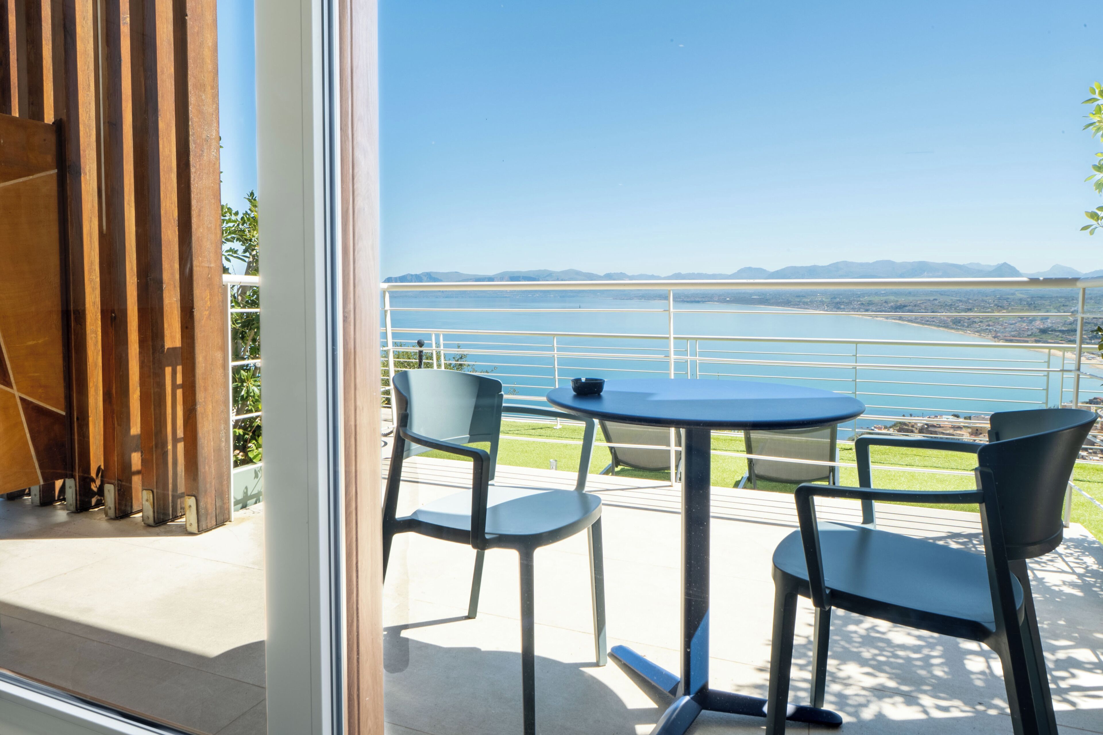 Een balkon met twee stoelen en een tafel, uitkijkend op een wateroppervlak en verre bergen.