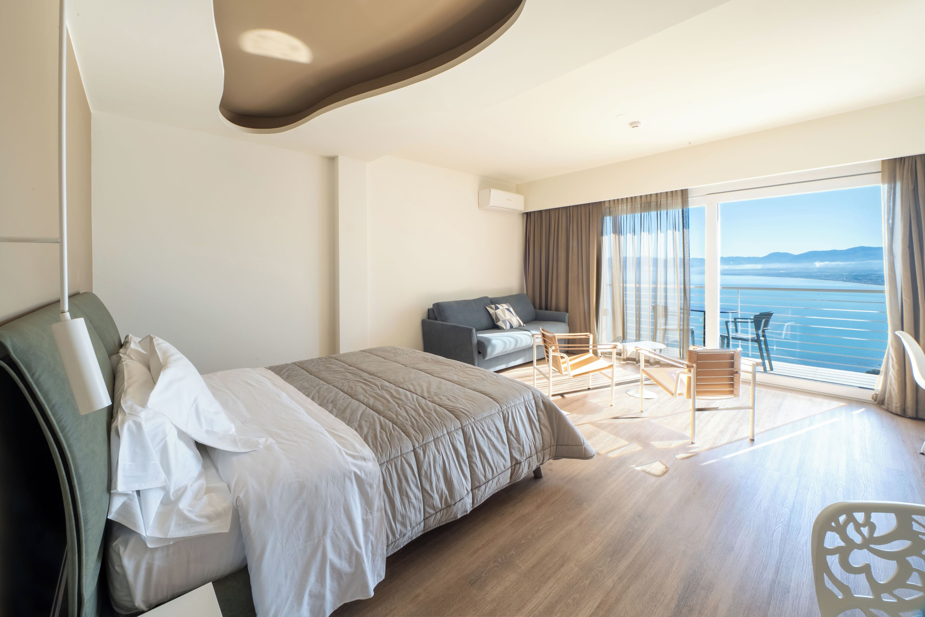 Una habitación de hotel con cama, sofá, balcón con vista al mar y zona de comedor.