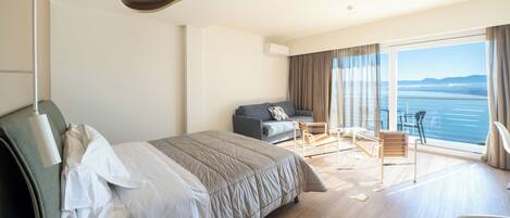 Una habitación de hotel con cama, sofá, balcón con vista al mar y zona de comedor.