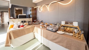 A breakfast buffet with various food items and beverages, a modern light fixture, and a kitchen area in the background. - Hotel Belvedere Resort 4 stelle (Castellammare del Golfo)