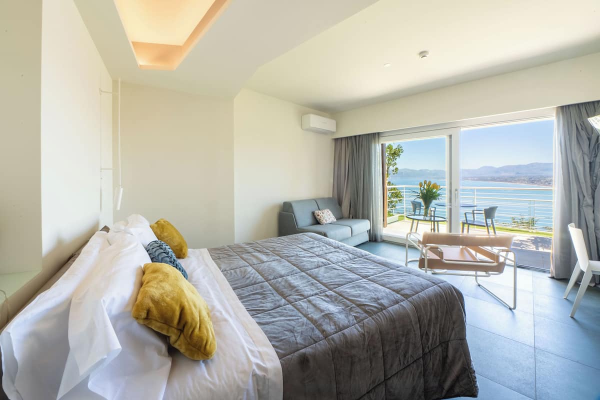 Ett hotellrum med en säng, en soffa, en balkong med ett bord och stolar samt utsikt över havet.