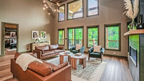 A spacious living room with a high ceiling, large windows, and a fireplace. - MMMajesty: Pool, View, Secluded, Theater, Games, Hot Tub, WiFi, Yard, Fire Pit (Sevierville)