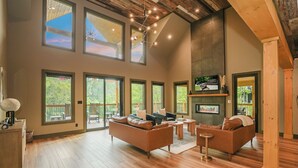 A spacious living room with large windows, a fireplace, and a wooden ceiling. - MMMajesty: Pool, View, Secluded, Theater, Games, Hot Tub, WiFi, Yard, Fire Pit (Sevierville)