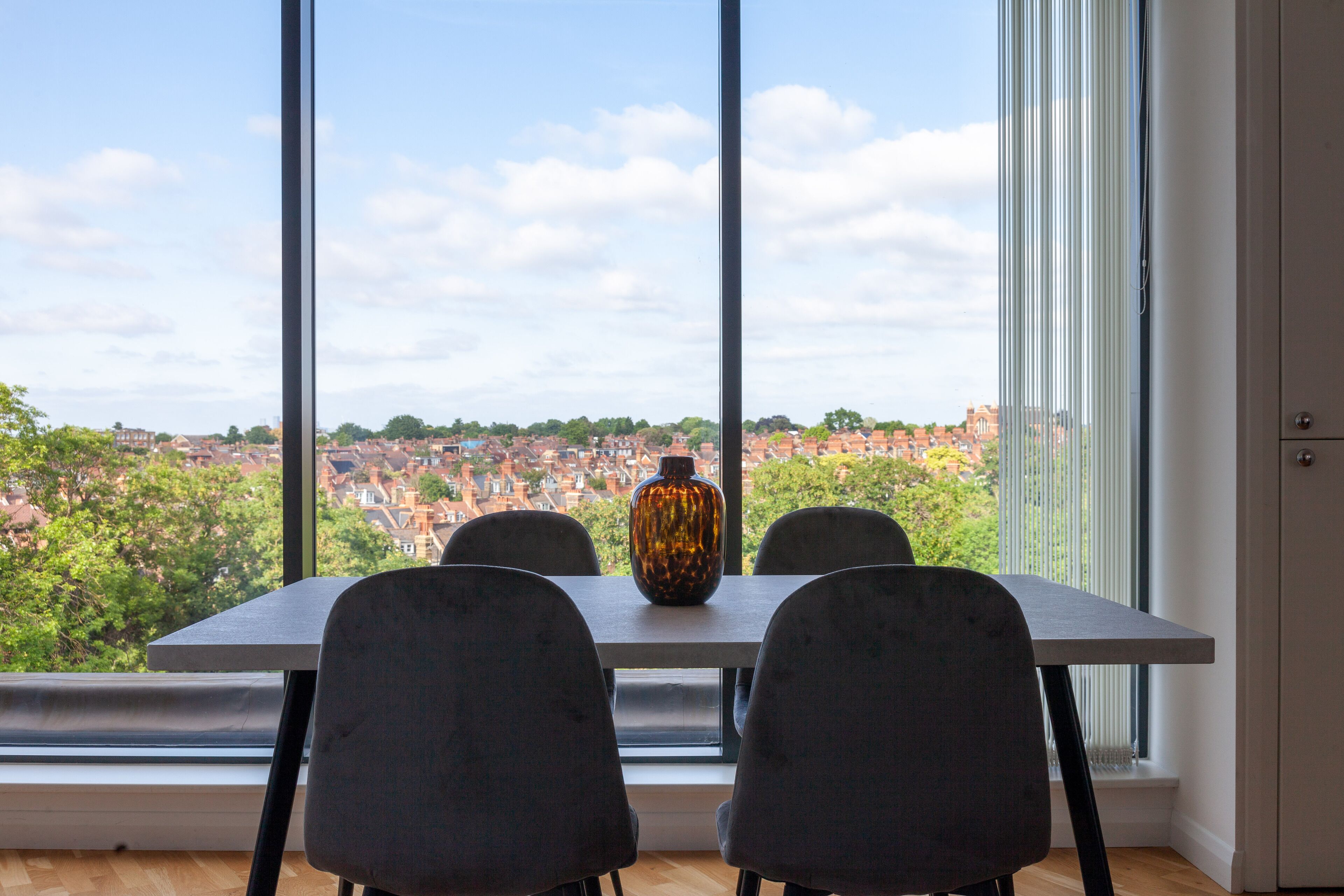 A dining area with a table and chairs, a vase, and a view of a cityscape through large windows.