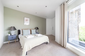 A bedroom with a bed, nightstands, a window with curtains, and a wall with a framed picture. - The Streatham Penthouse (London)