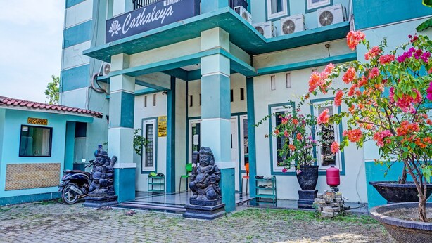A building with a sign reading "Cathaleya" and a security sign. There are two statues in front, a motorcycle parked to the left, and potted plants with flowers. - Hotel O Home Stay Elis Cateliya Syariah (Karawang)