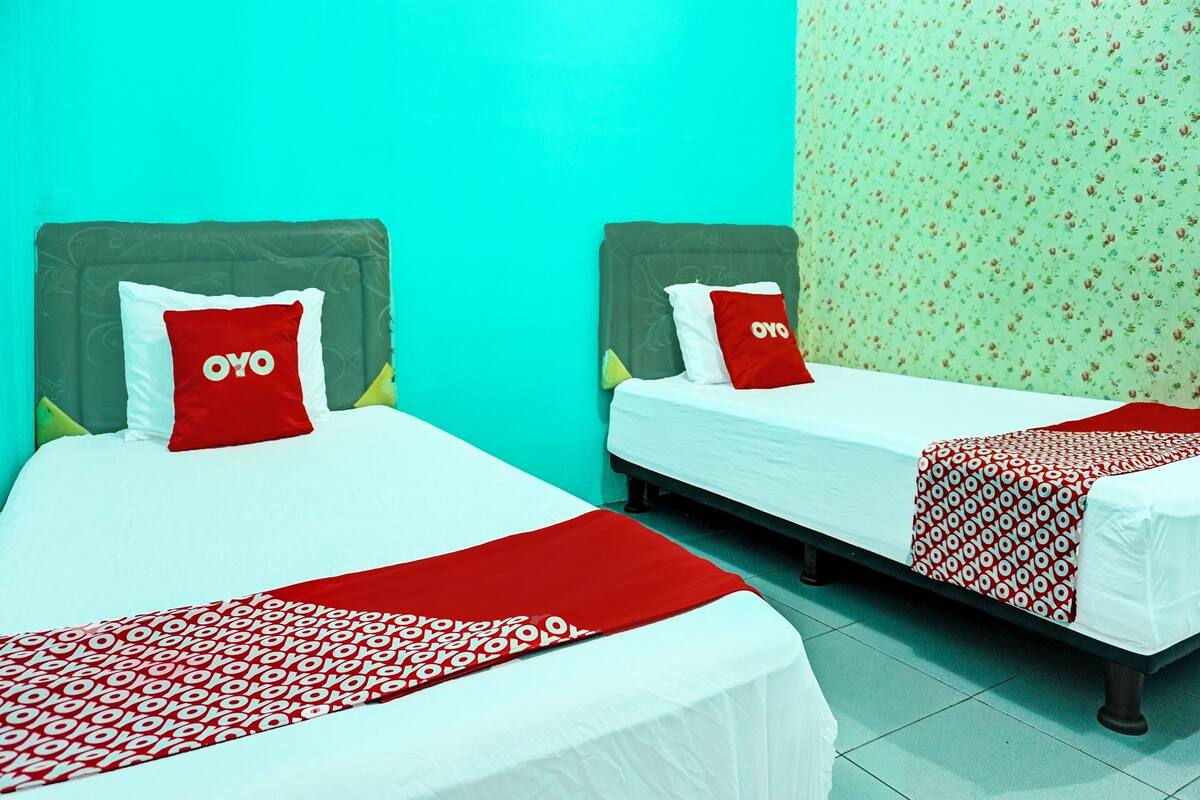 Dos camas individuales con ropa de cama roja y blanca, un cabecero verde y un papel tapiz con motivos florales.