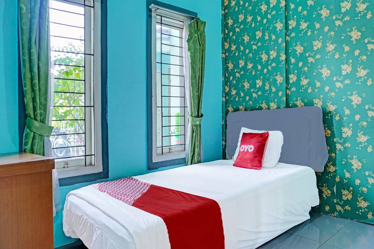 Un dormitorio con una cama, un escritorio de madera y dos ventanas con cortinas.