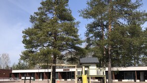 A playground with a yellow slide and swings, surrounded by trees and a building with a sign that reads "Stad La Vie". - Leikari Bungalows (Kotka)