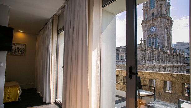 A hotel room with a balcony, a bed, a chair, and a view of a historic clock tower. - 262 Boutique Aliados (Porto)