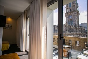 Ett hotellrum med en balkong, en säng, en stol och utsikt över ett historiskt klocktorn.