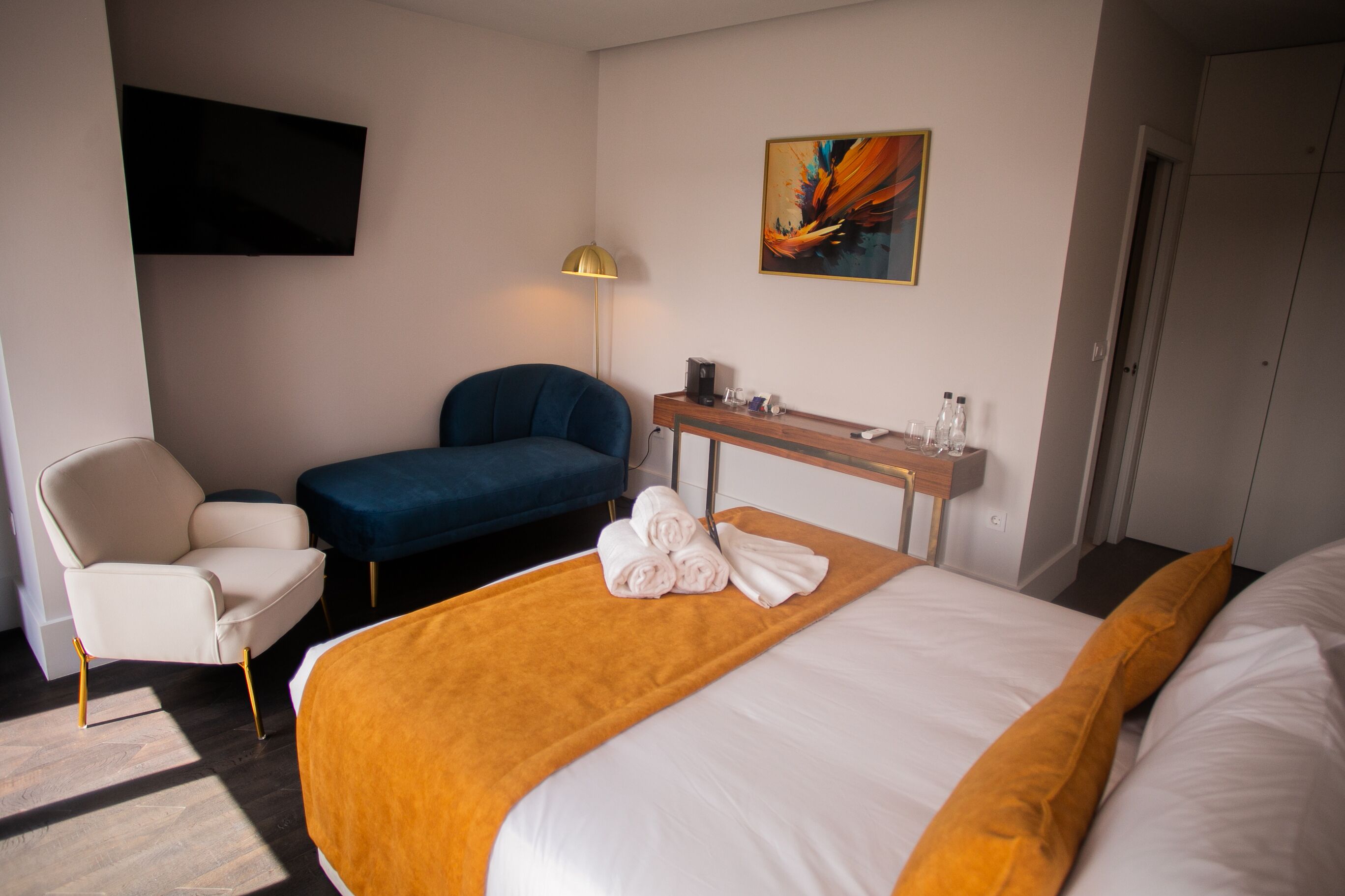 A hotel room with a bed, a desk, a chair, a TV, and a painting on the wall.