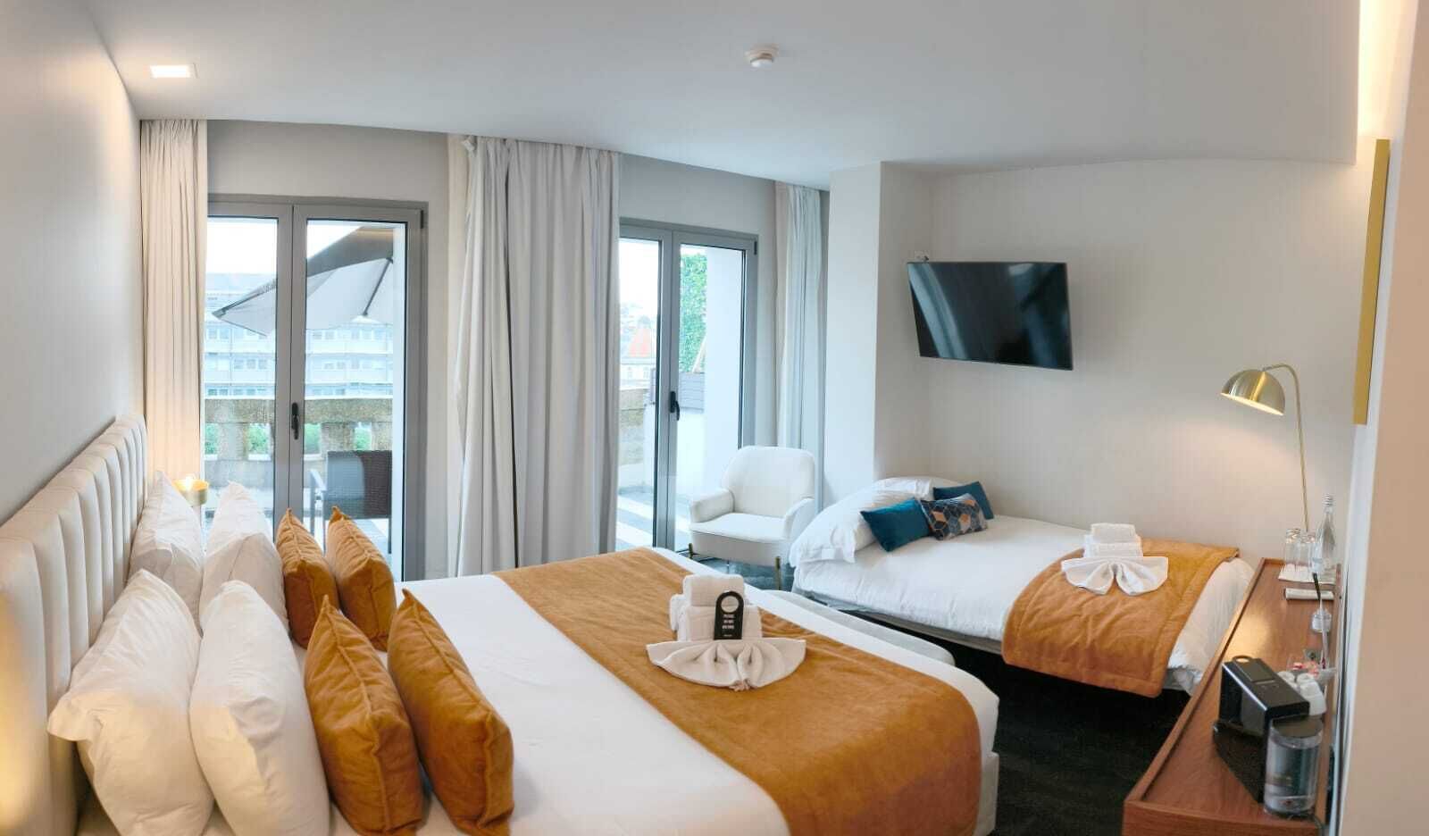 A hotel room with two beds, a TV, a desk with a lamp, and a view through the glass door.