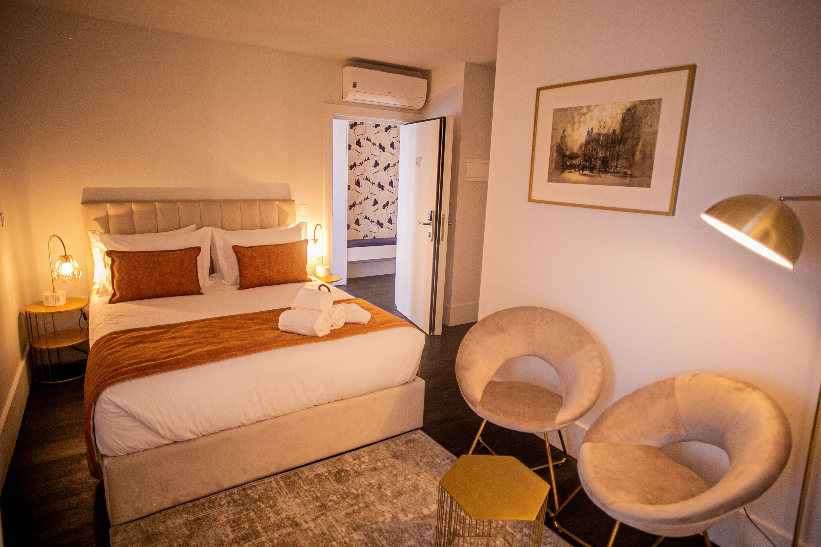A hotel room with a large bed, bedside lamps, a chair, and a framed picture on the wall.