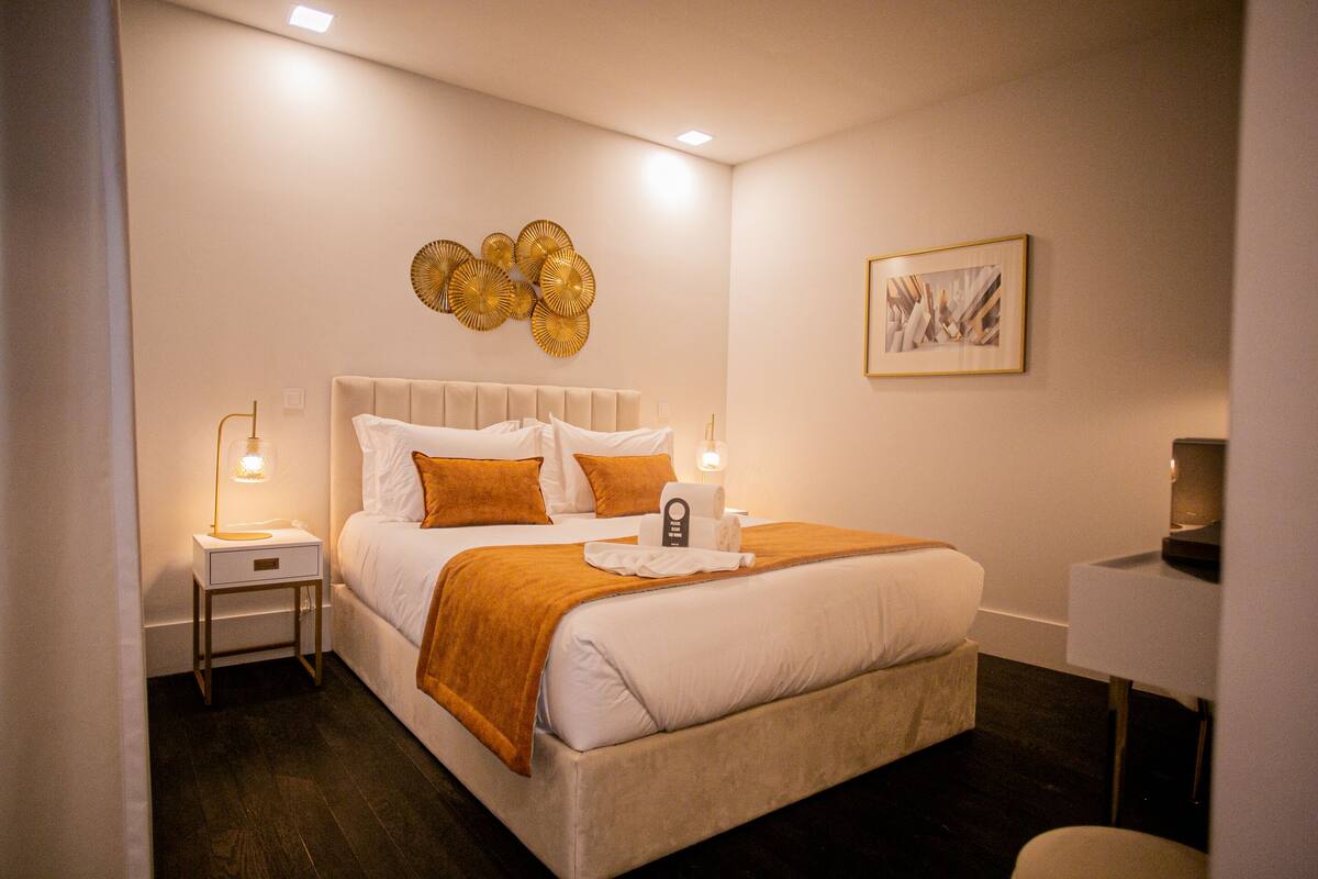 Une chambre d’hôtel avec un grand lit, deux tables de chevet, une commode, une lampe de chevet, une œuvre d’art murale et un tableau encadré.