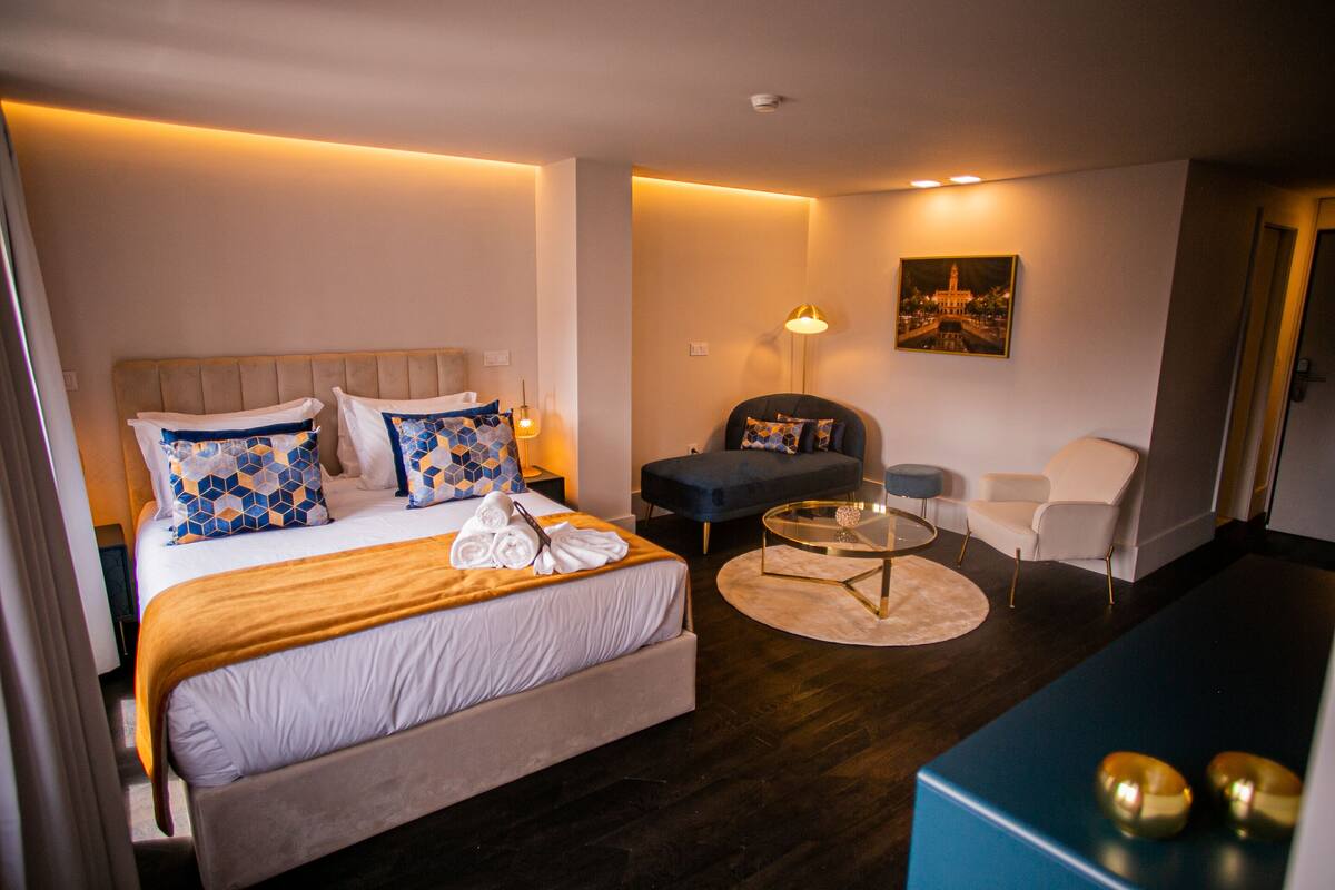 Une chambre d’hôtel avec un lit, un canapé, une chaise, une petite table et un tableau au mur.