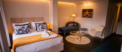 A hotel room with a bed, a sofa, a chair, a small table, and a painting on the wall.