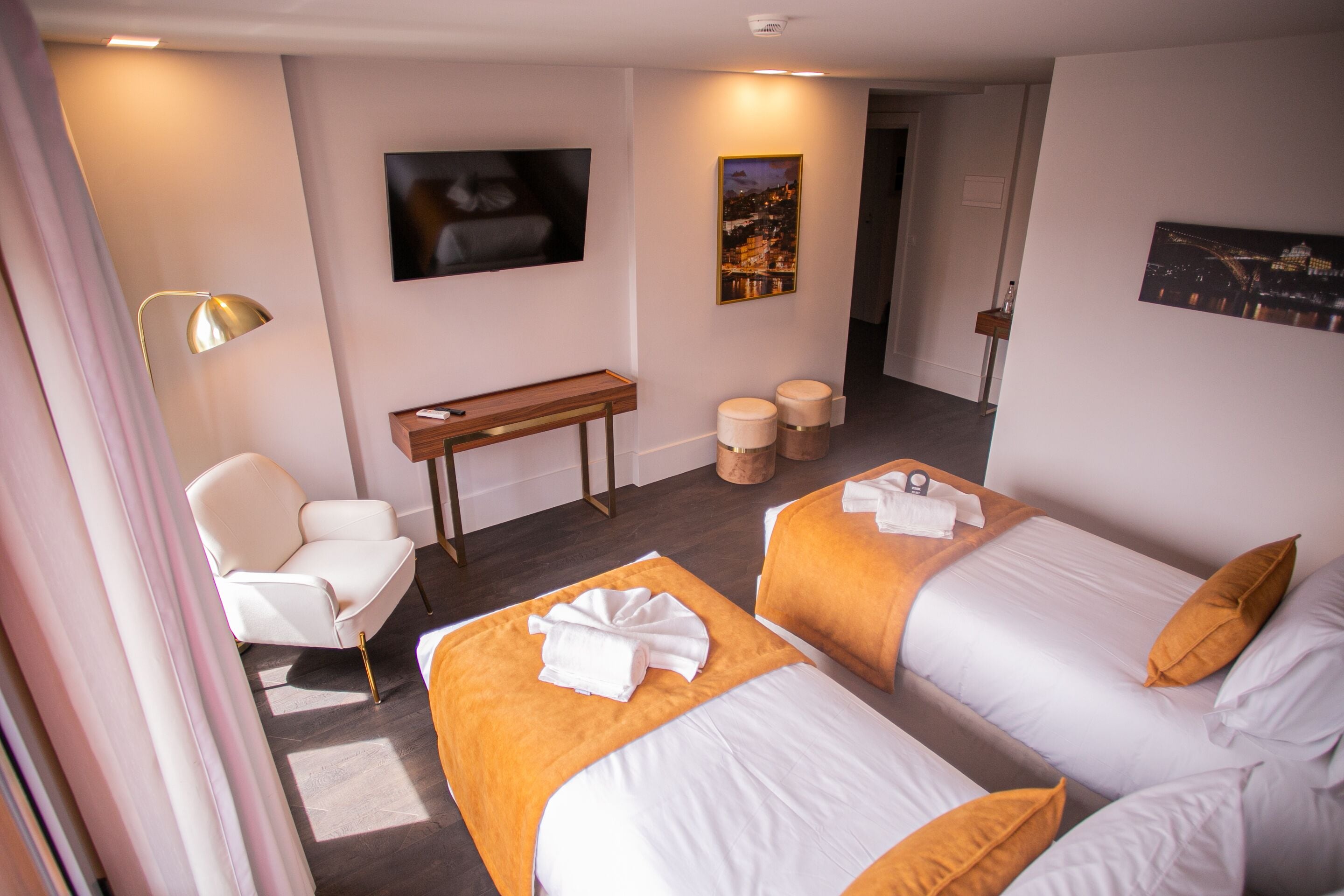 A hotel room with two beds, a desk, a chair, a TV, and a painting on the wall.