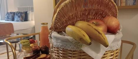 A wicker basket filled with fruits and bread on a table, with a bottle of juice and a plate of bread slices nearby.