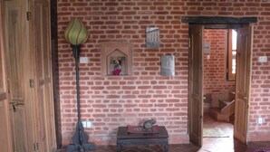 Une pièce avec un mur en briques, des portes en bois, une petite table sur laquelle est posée une figurine, et une lampe.