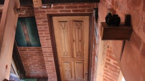 Une porte en bois ornée de sculptures complexes, un mur de briques et une petite étagère sur laquelle sont posés divers objets.
