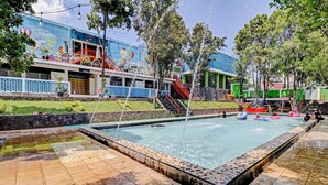 Una piscina con tobogán de agua, rodeada por un solárium con baldosas y un mural.