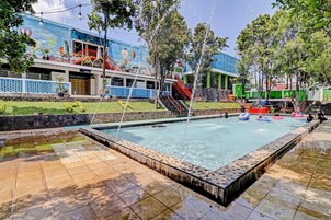 A swimming pool with a water slide, surrounded by a tiled deck and a mural.