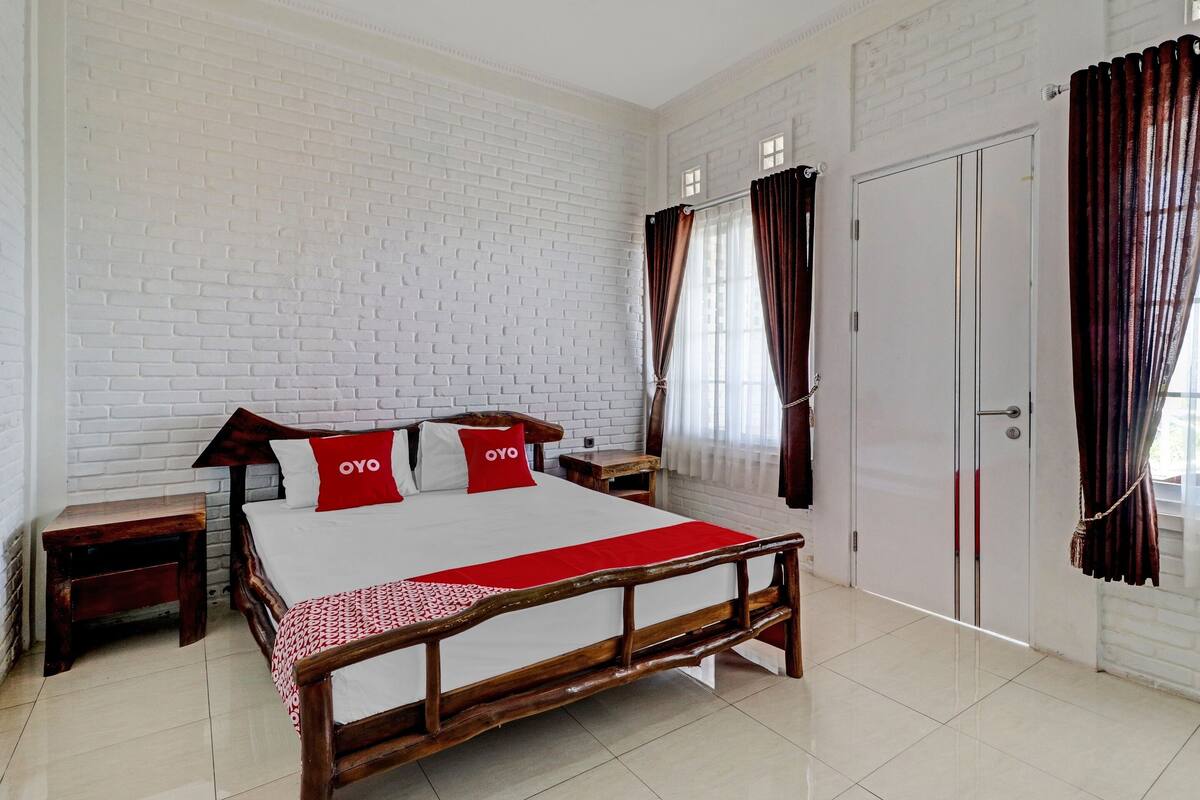 A bedroom with a wooden bed, white brick walls, a white door, and brown curtains.