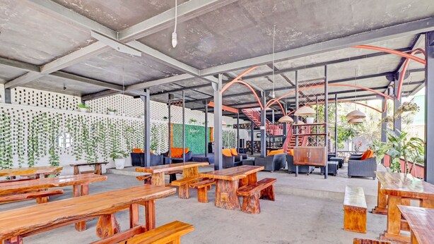 Un café al aire libre con mesas y bancos de madera, techo de hormigón y vistas al exterior.