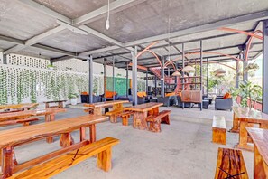 An open-air café with wooden tables and benches, a concrete ceiling, and a view of the outdoors. - Collection O 90617 Rumah Oma Opa Syariah (Bandung)