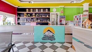 Zona de recepción con mostrador de registro, estanterías con diversos artículos, un reloj y una pared verde con un mural alusivo a la cocina.